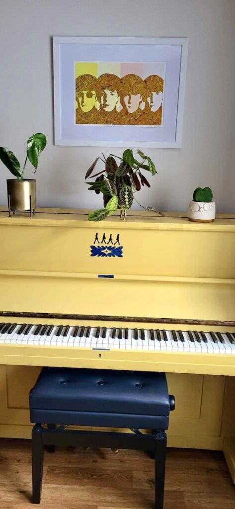 The Beatles By Kerwin framed print next to a yellow piano